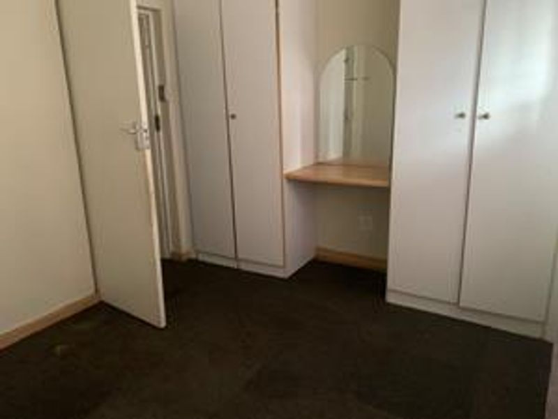 Bedroom featuring built-in cupboards and a integrated vanity station with a mirror, requiring cosmetic updates to flooring and finishes.