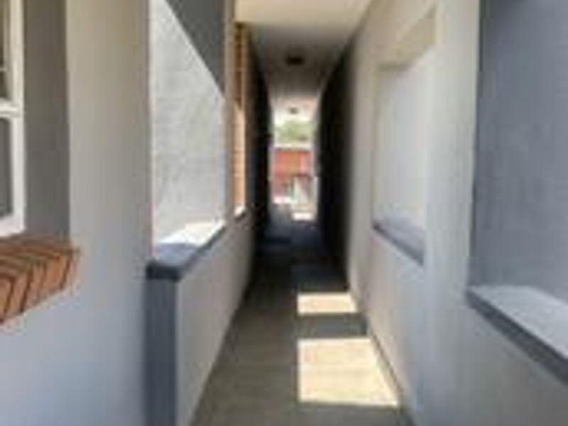 A clean, well-maintained apartment hallway featuring neutral grey walls, tiled flooring, and recessed ceiling lighting.