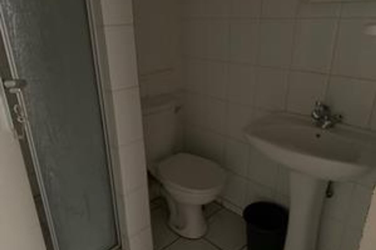 A functional bathroom featuring a pedestal sink, toilet, and a shower enclosure with tiled walls and flooring.