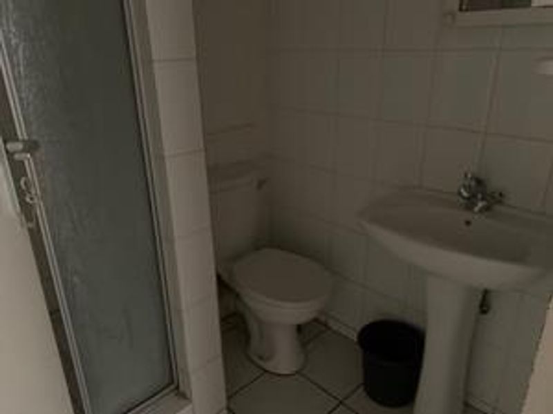 A functional bathroom featuring a pedestal sink, toilet, and a shower enclosure with tiled walls and flooring.