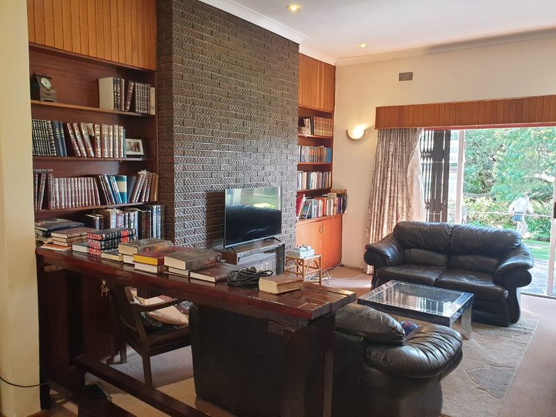 Spacious living room featuring a prominent brick fireplace, extensive built-in wooden cabinetry, and direct access to the garden through sliding glass doors.