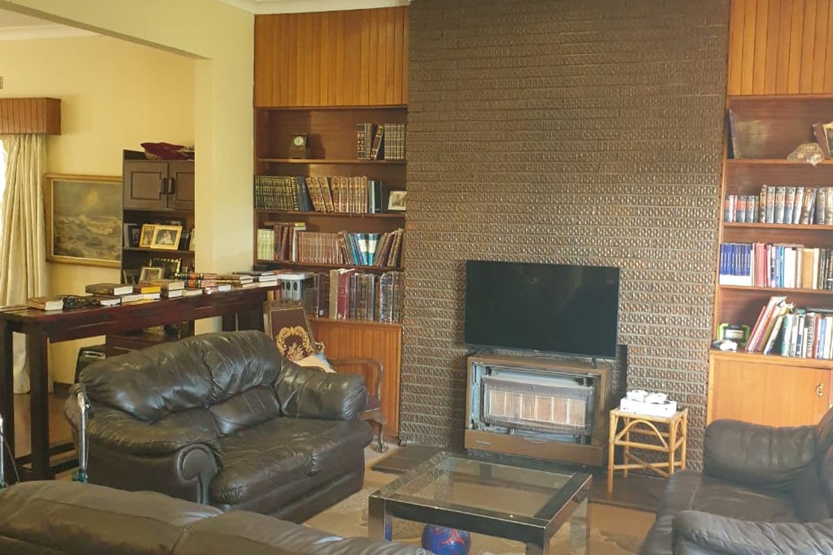 A living room featuring a prominent brick fireplace, built-in wooden shelving, and wood paneling, offering a traditional and cozy atmosphere.