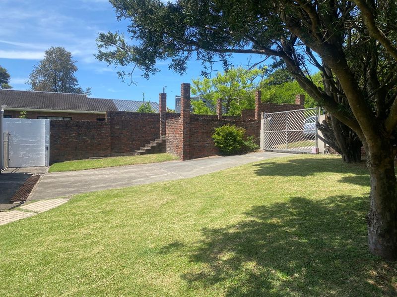 Front exterior view featuring a concrete driveway, lawn, and a brick boundary wall with a metal gate.