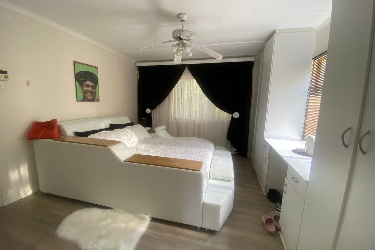 A well-maintained bedroom featuring laminate flooring, built-in cupboards, and a ceiling fan, offering a functional and comfortable living space.