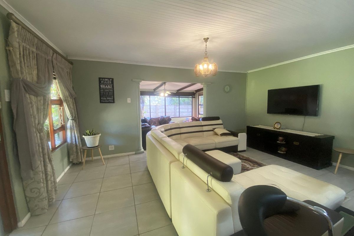 A spacious living room featuring tiled flooring, a tongue and groove ceiling, and a wall-mounted television, with an open flow to an adjacent area.