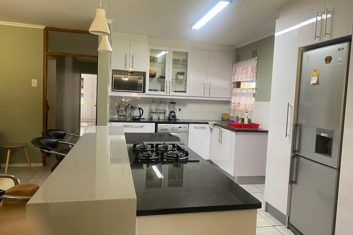 A functional kitchen featuring white cabinetry, granite countertops, a central island with a gas hob, and tiled flooring.