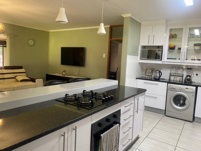 Open-plan kitchen and living area featuring modern white cabinetry, granite countertops, a gas hob, built-in oven, and tiled flooring throughout.