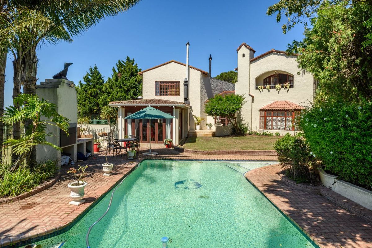 Rear view of the property featuring a swimming pool, built-in braai area, and established garden with traditional architectural styling.