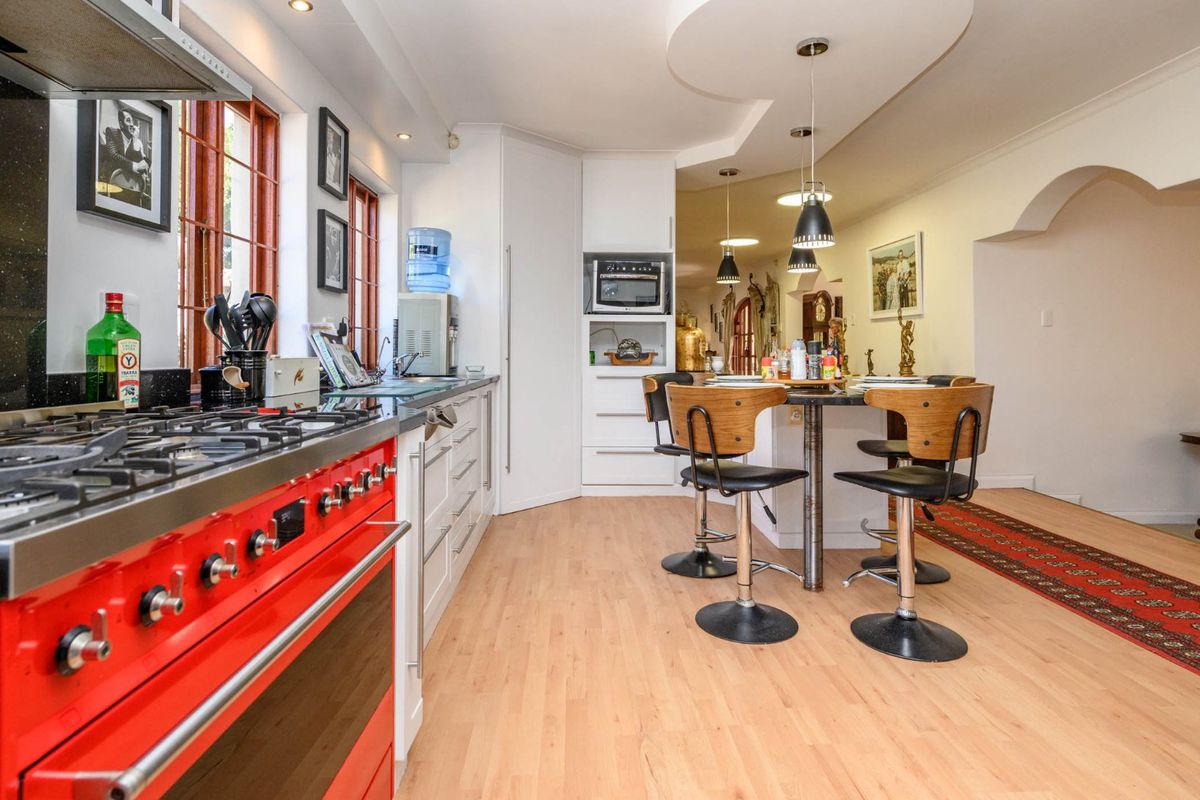 A well-appointed kitchen featuring a striking red gas range cooker, modern cabinetry, stone countertops, and a central breakfast bar with pendant lighting.