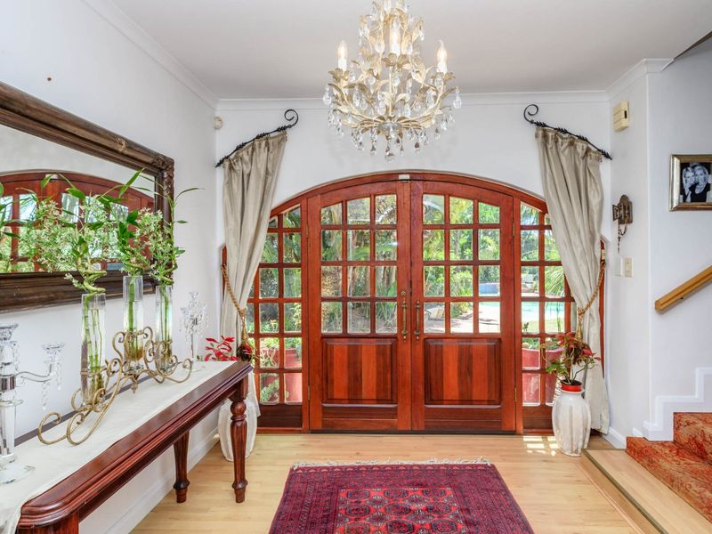 Elegant entrance foyer featuring arched timber double doors, polished timber flooring, and a decorative chandelier, providing a welcoming transition to the home.