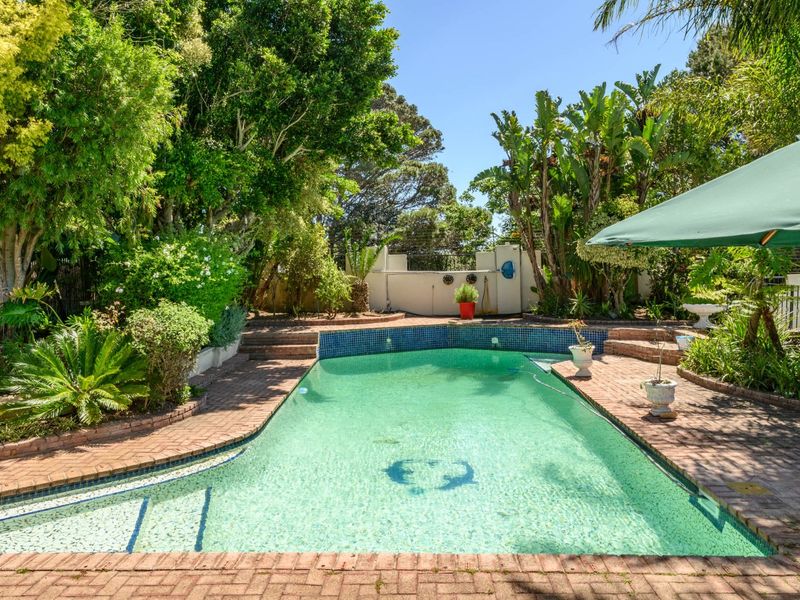 A private swimming pool area surrounded by established trees and lush garden landscaping, featuring brick paved surrounds and a retaining wall.