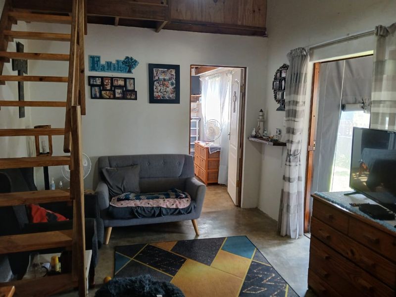 A living room featuring concrete flooring, a wooden staircase leading to a loft area, and a sliding glass door providing access to the exterior.