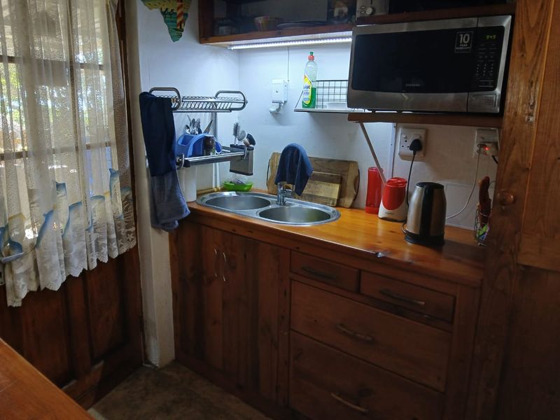 A compact scullery area featuring wooden cabinetry, a double bowl stainless steel sink, and built-in microwave shelving with under-cabinet lighting.