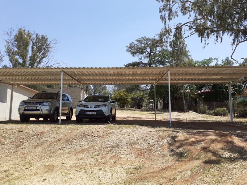 A functional outdoor metal carport structure providing covered parking space on a rural property.