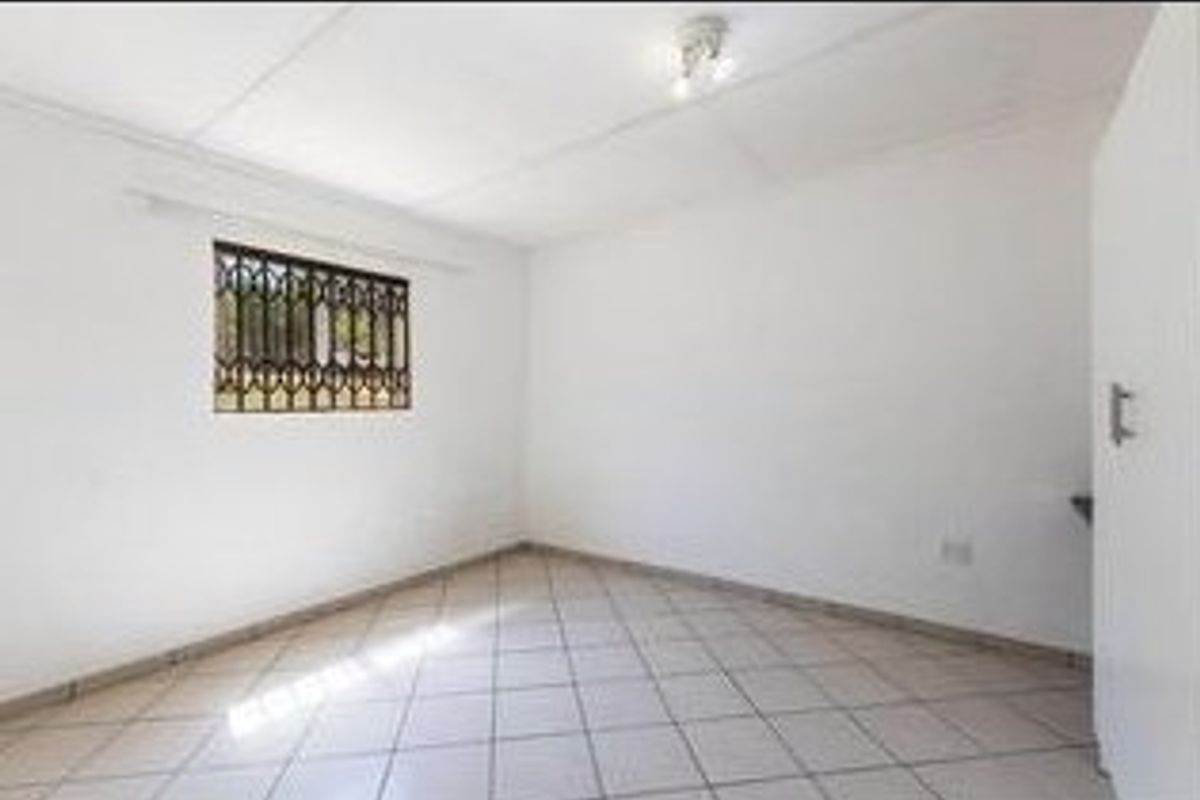 A clean, empty bedroom featuring tiled flooring, a security gate on the window, and a built-in cupboard.