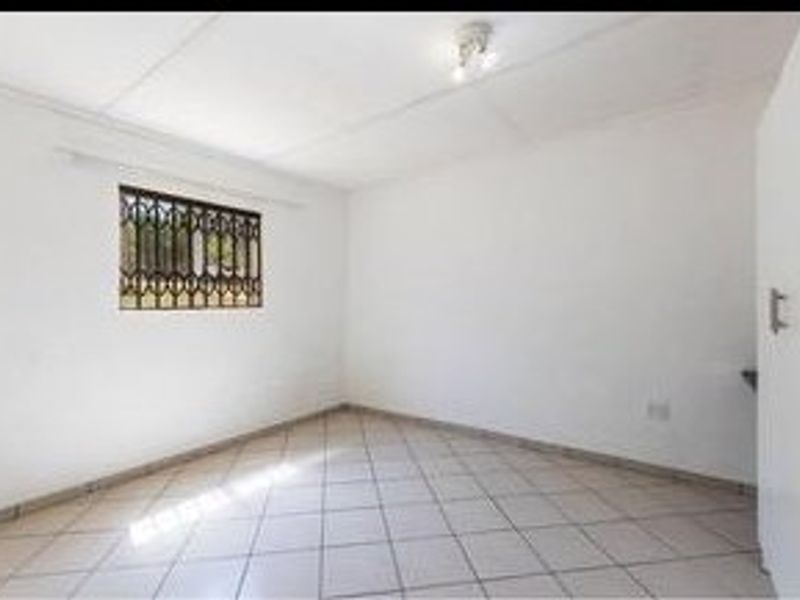 A clean, empty bedroom featuring tiled flooring, a security gate on the window, and a built-in cupboard.