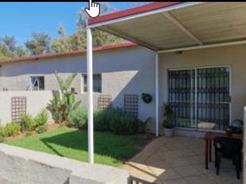 A covered patio area featuring tiled flooring and a sliding glass door with security gate, overlooking a small private garden.