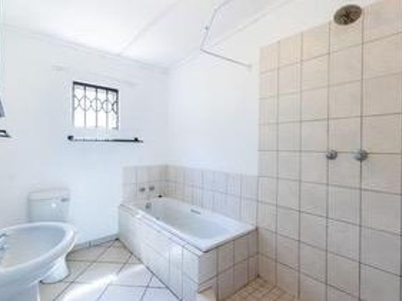 A functional bathroom featuring a pedestal basin, a built-in bathtub, and a tiled shower area with a wall-mounted shower head.