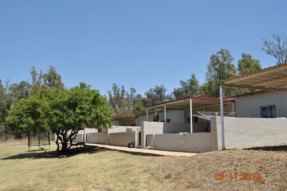 Rear view of the farm property showing a series of covered patios with low masonry walls and a concrete walkway.