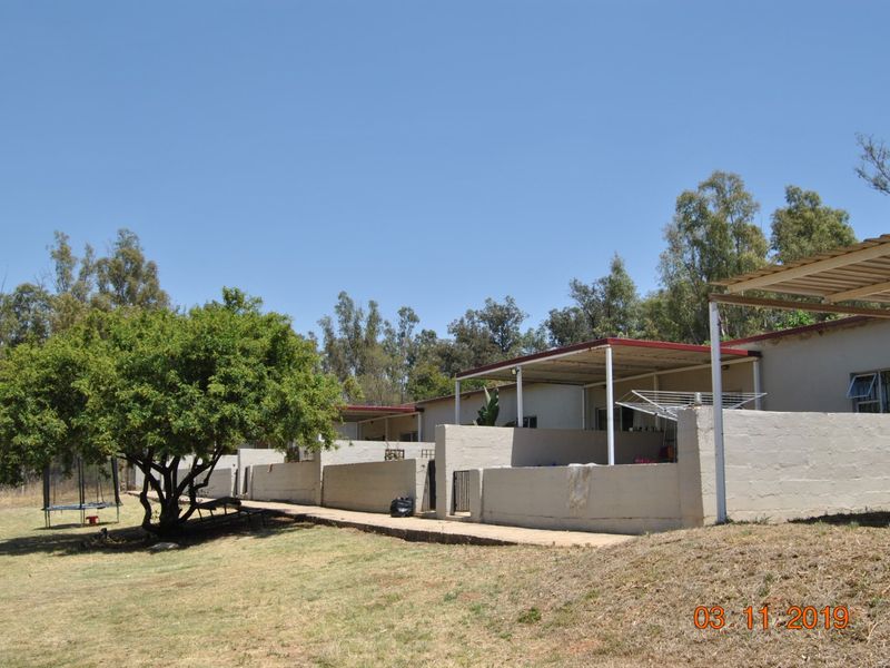 Rear view of the farm property showing a series of covered patios with low masonry walls and a concrete walkway.