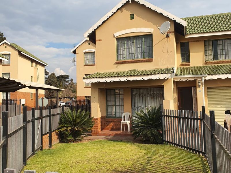 Front view of a two-story townhouse featuring a small private garden, metal fencing, tiled roof, and a single garage.