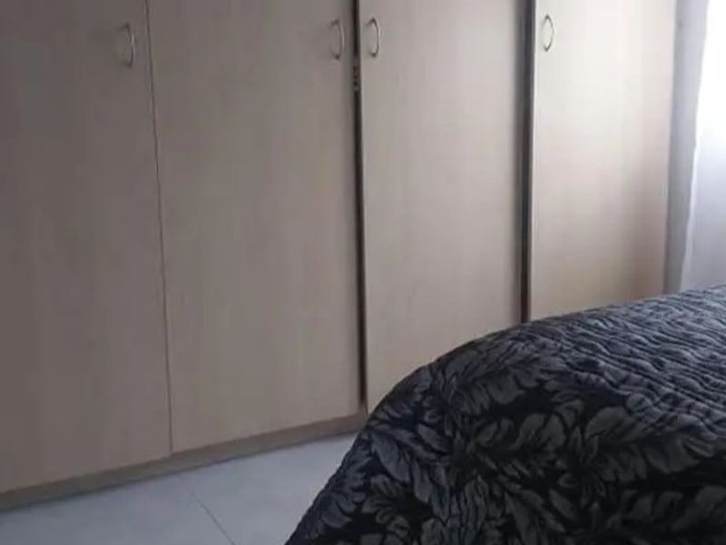 A bedroom featuring light-toned built-in cupboards with modern handles and tiled flooring.