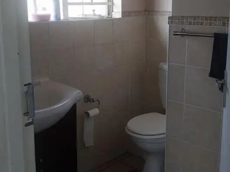 A compact bathroom featuring a vanity basin, toilet, and tiled finishes, illuminated by a window with security bars.