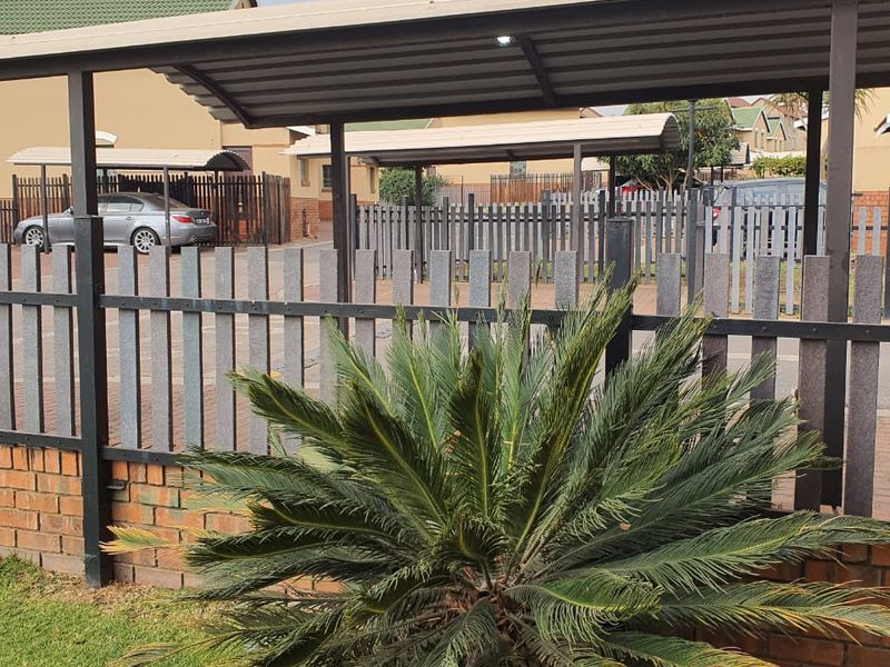 Front exterior view of the townhouse featuring a covered carport, brick and picket fencing, and paved driveway access.