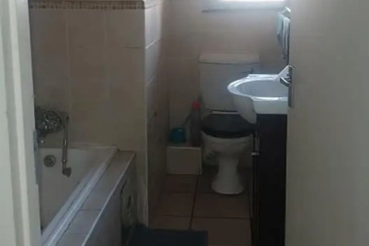 A compact bathroom featuring a bathtub, toilet, and vanity with tiled flooring and wall finishes, requiring cosmetic updates to modernize the space.