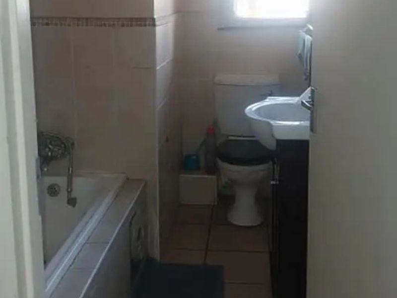 A compact bathroom featuring a bathtub, toilet, and vanity with tiled flooring and wall finishes, requiring cosmetic updates to modernize the space.