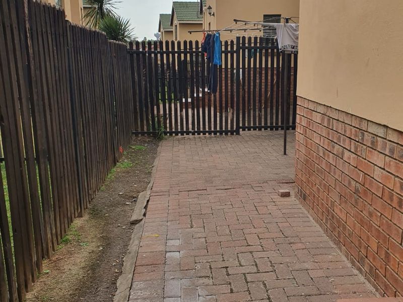 A side walkway of a townhouse featuring brick paving, a timber boundary fence, and a brick-accented exterior wall.