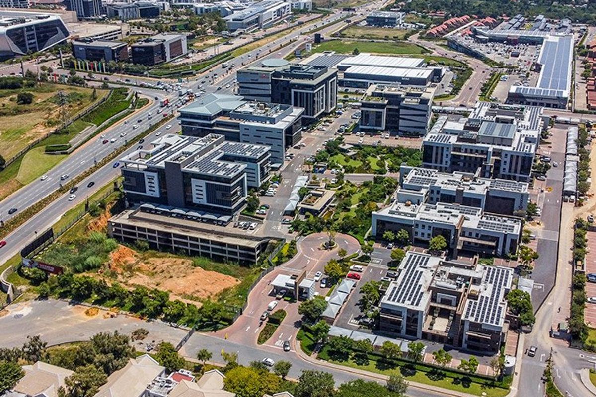 Aerial view of a modern commercial office park featuring multiple buildings, extensive parking facilities, solar panel installations, and landscaped green spaces.