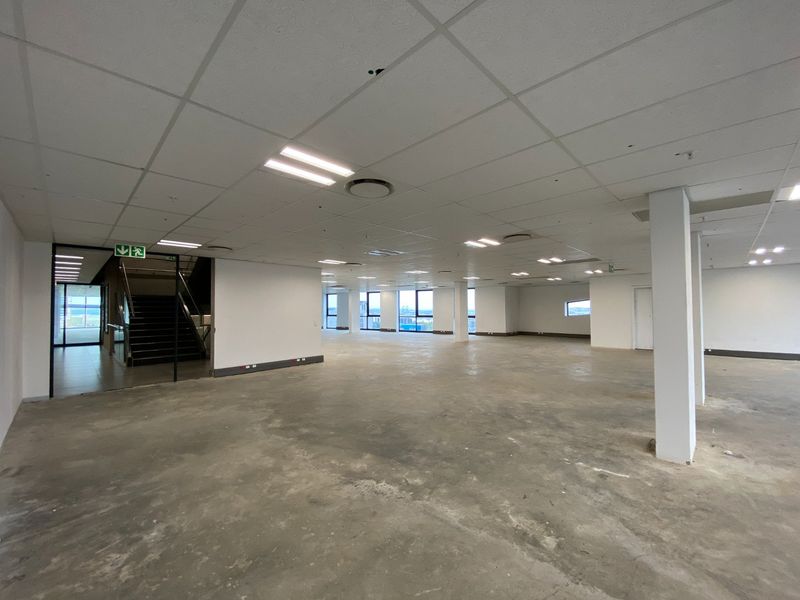 A large, open-plan commercial office space featuring concrete flooring, suspended ceilings, and structural columns, offering a blank canvas for custom fit-outs.