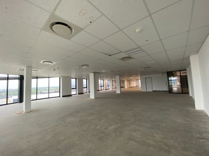 Spacious open-plan commercial office area featuring large floor-to-ceiling windows, suspended ceilings with integrated air conditioning, and an unfinished concrete floor.