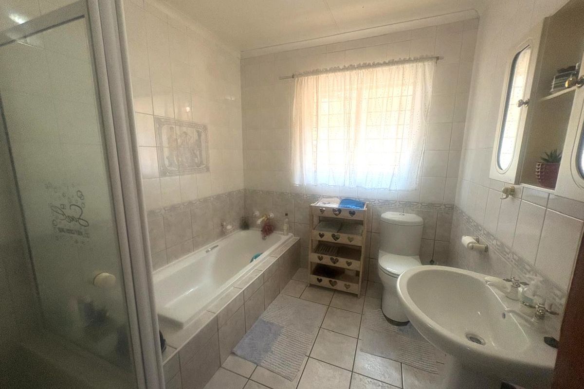 A functional bathroom featuring a built-in bathtub, separate shower enclosure, pedestal basin, and toilet with neutral wall and floor tiling.