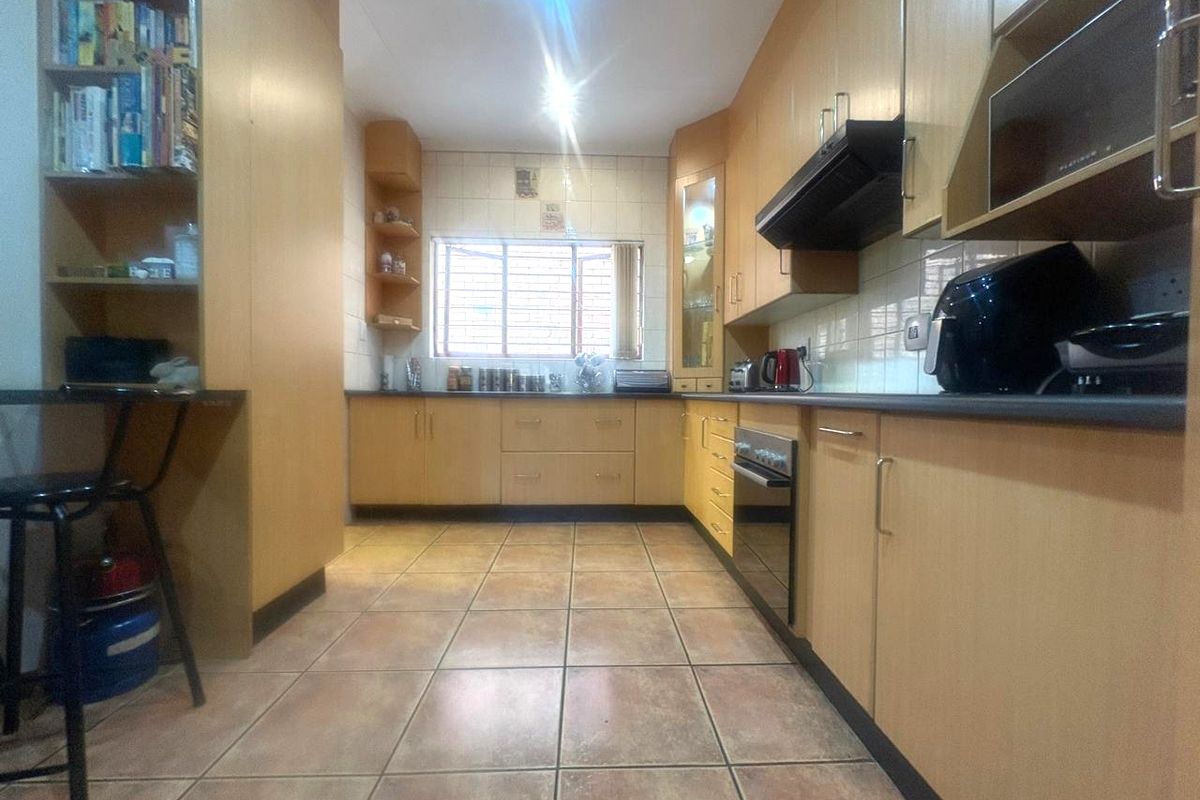 A functional kitchen featuring light wood-tone cabinetry, tiled flooring, a built-in oven with extractor fan, and ample storage space with integrated shelving.