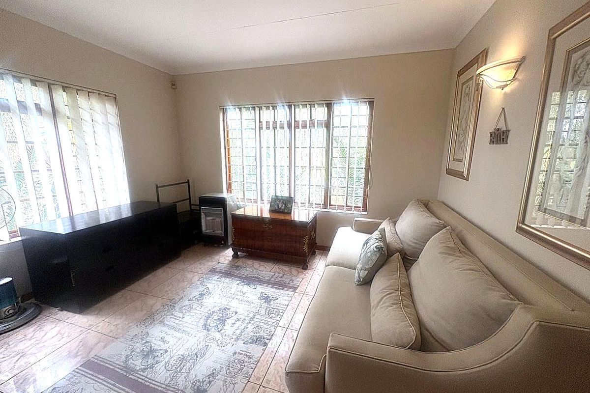 A comfortable living room featuring tiled flooring, large windows with security bars, and wall-mounted lighting, offering a functional and well-lit space.