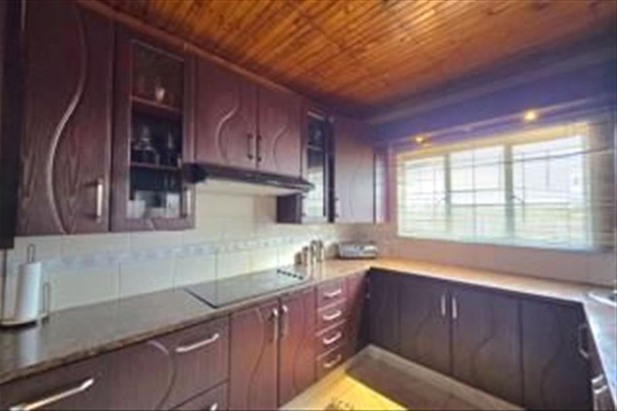 A dated kitchen featuring dark wood-look cabinetry, laminate countertops, a built-in hob with extractor fan, and a timber-paneled ceiling.