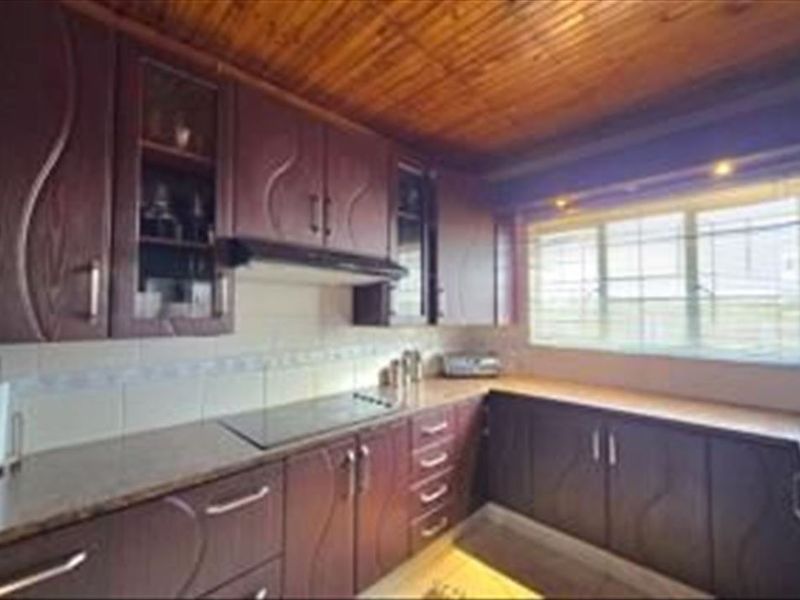 A dated kitchen featuring dark wood-look cabinetry, laminate countertops, a built-in hob with extractor fan, and a timber-paneled ceiling.