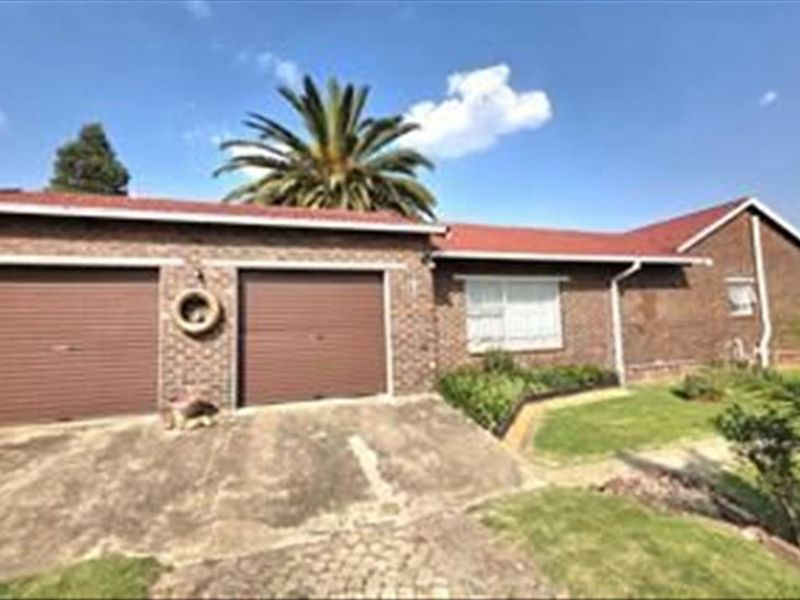 Front exterior view of a brick house featuring a double garage, concrete driveway, and established garden area.