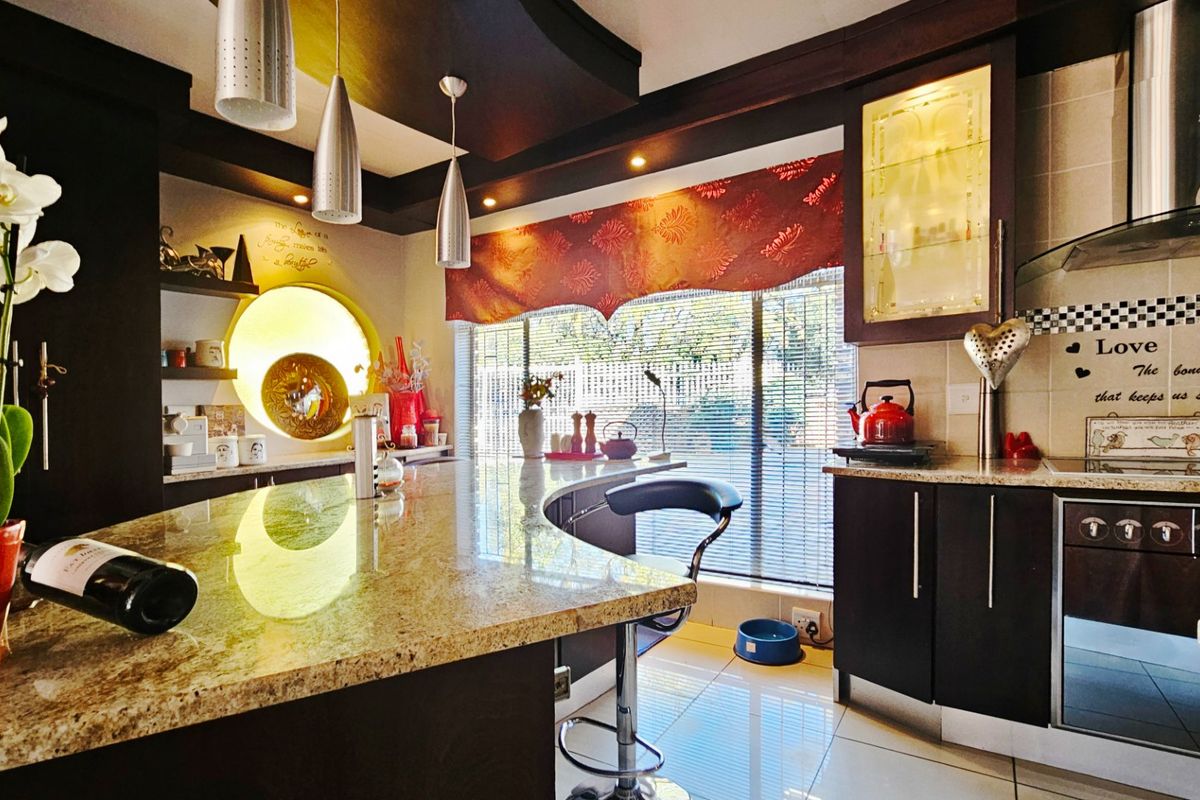 Modern kitchen featuring granite countertops, dark cabinetry, a breakfast bar, integrated extractor fan, and tiled flooring with ample natural light.