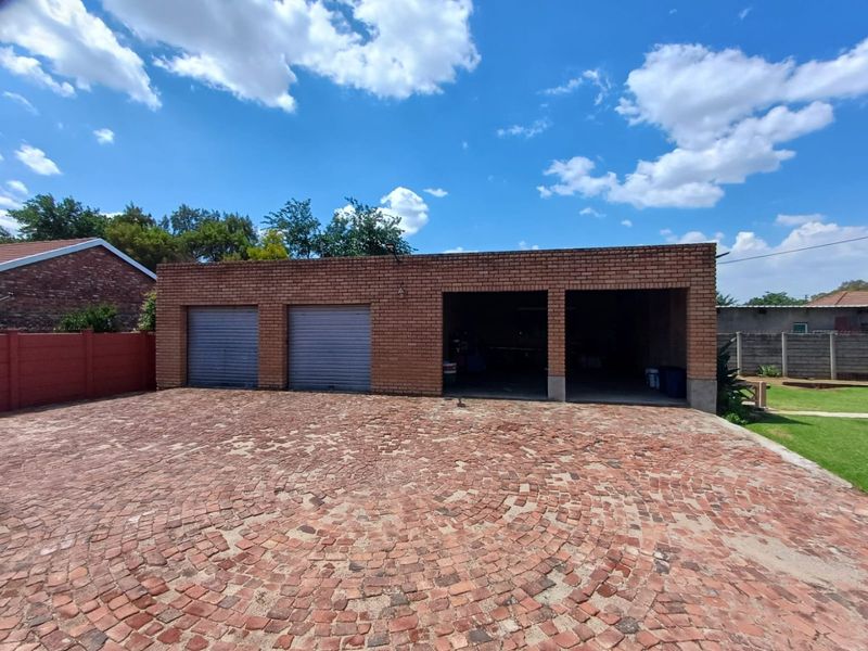 A multi-bay garage structure featuring a combination of enclosed roller shutter doors and open bays, set against a large brick-paved driveway.