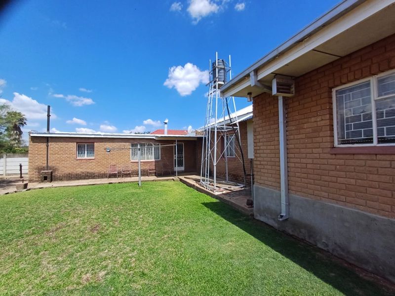 Rear view of the house featuring a face brick exterior, a water tank stand, and a well-maintained lawn area.