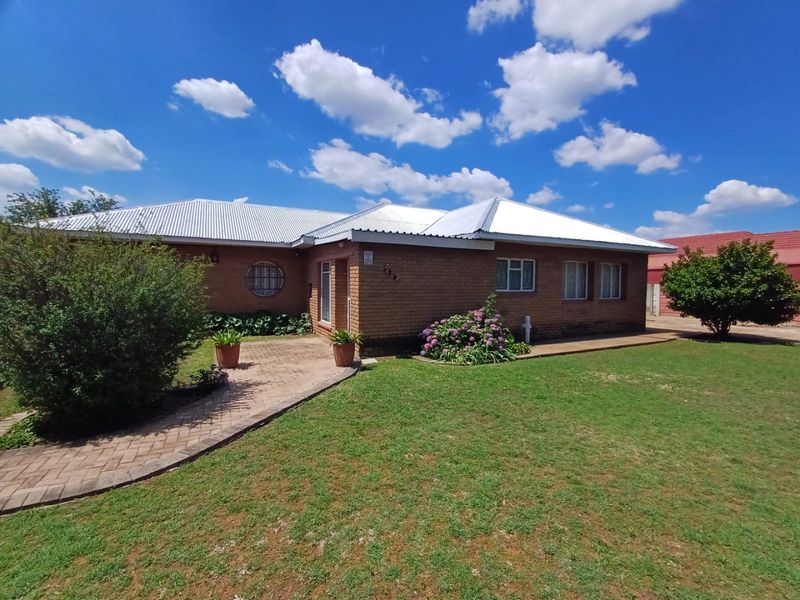 A well-maintained single-story brick house featuring a corrugated metal roof, a paved front walkway, and established garden landscaping.