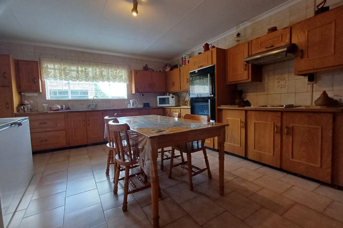 Spacious kitchen featuring traditional wooden cabinetry, built-in oven, extractor fan, tiled backsplash, and tiled flooring with ample space for a dining table.
