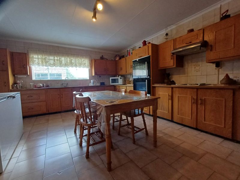 Spacious kitchen featuring traditional wooden cabinetry, built-in oven, extractor fan, tiled backsplash, and tiled flooring with ample space for a dining table.