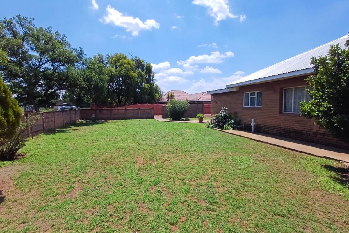 A spacious rear garden featuring a well-maintained lawn, brick boundary walls, and a concrete pathway along the side of the brick house.