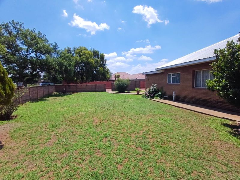 A spacious rear garden featuring a well-maintained lawn, brick boundary walls, and a concrete pathway along the side of the brick house.