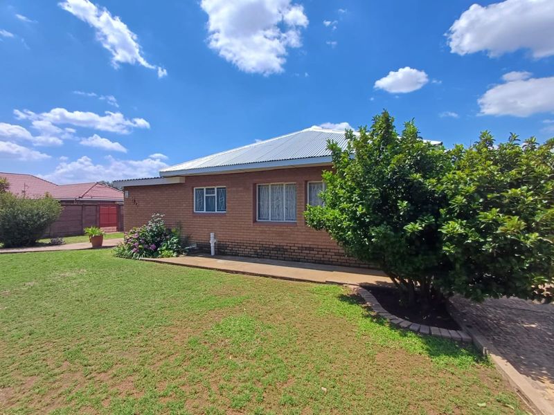 A view of the front elevation of a brick house featuring a corrugated metal roof, security-barred windows, and a well-maintained lawn.