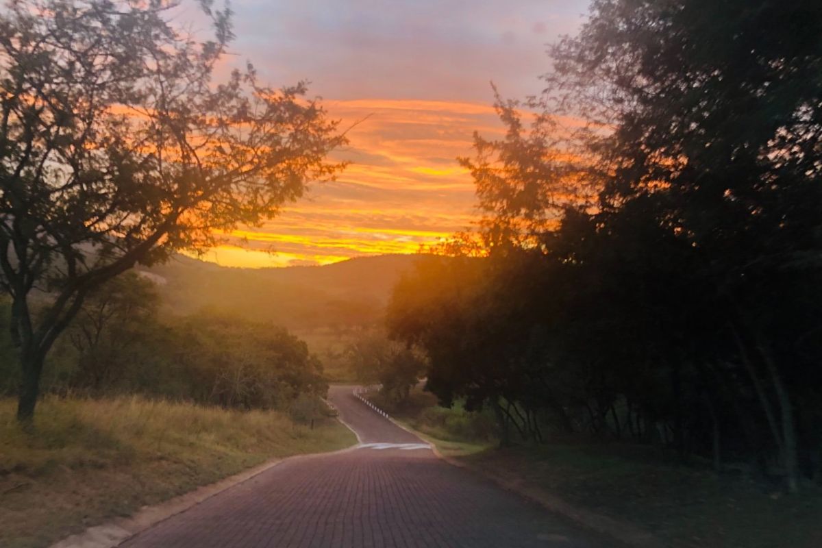A scenic view of a paved road winding through a natural landscape at sunset, showcasing the property's surroundings and access.